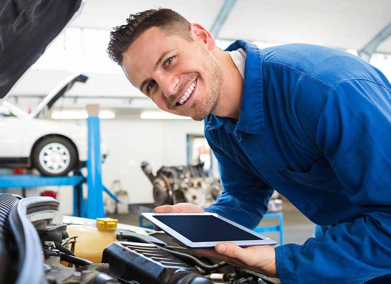 Service technician holding ipad looking at car engine